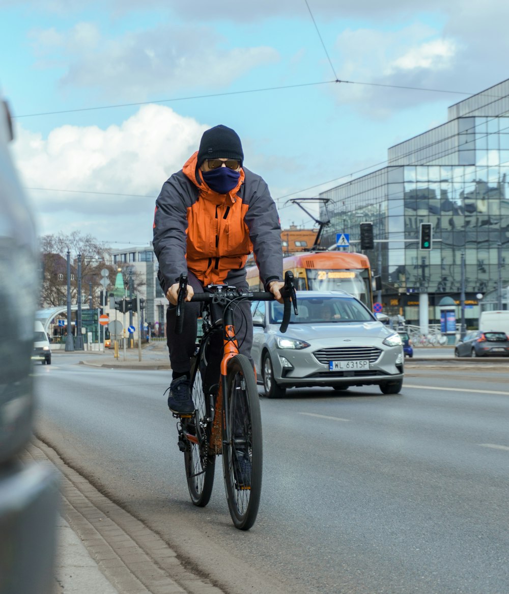 man in orange jacket riding bicycle on road during daytime