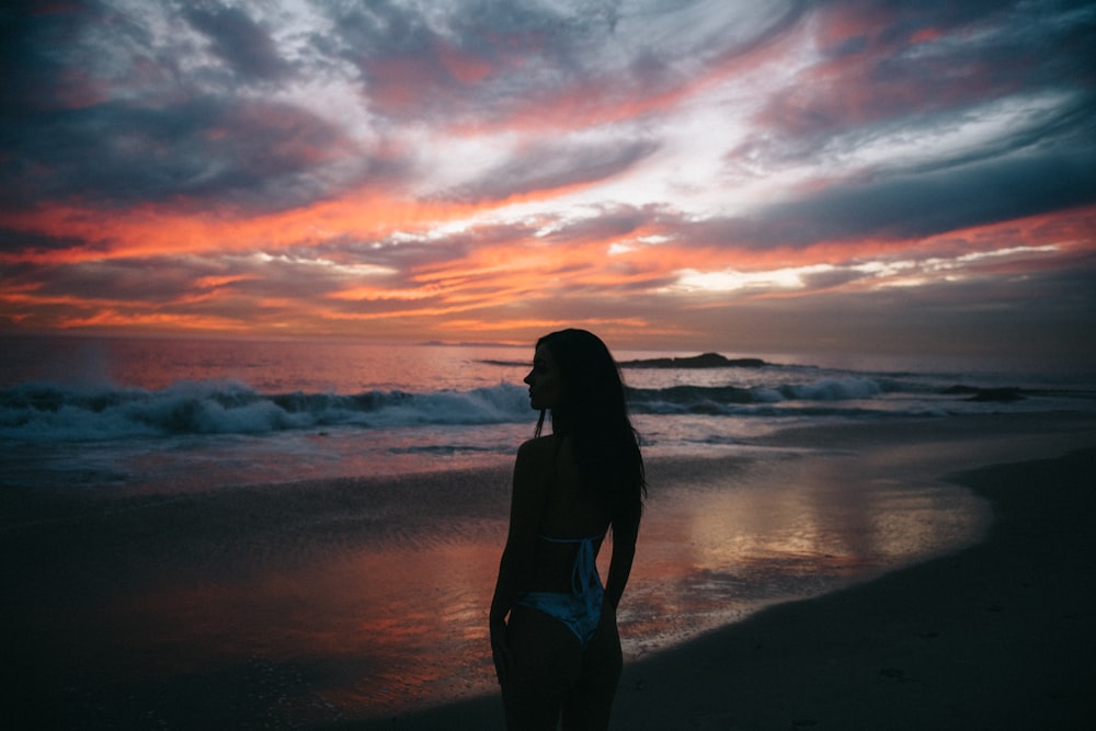 woman in black bikini standing on beach during sunset