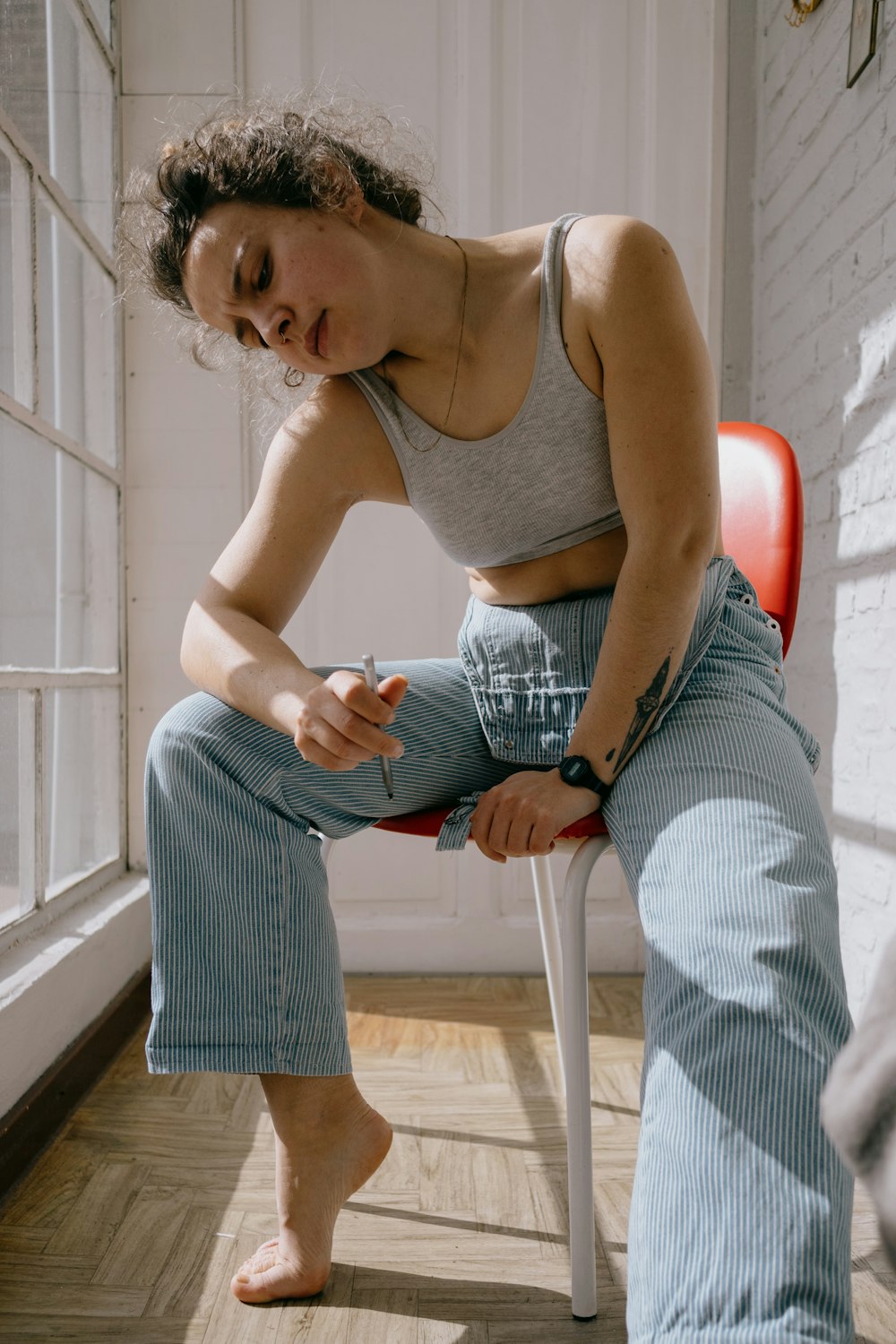 woman in white tank top and blue and white striped pants sitting on orange plastic chair