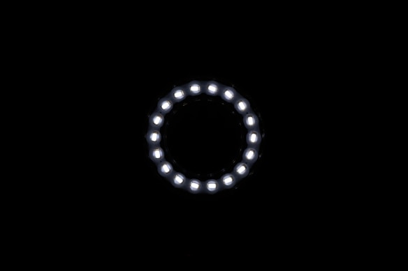 A circular array of white LED lights shines against a dark background, forming a glowing ring. The uniform lights create a sense of symmetry and focus.