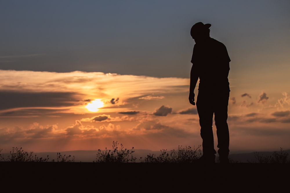 silhouette of man standing on grass field during sunset