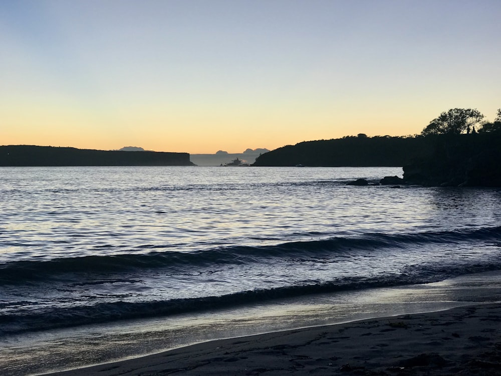 body of water near mountain during sunset