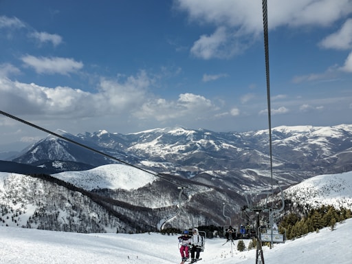 A friendly ski guide carrying children’s ski gear uphill with snowy mountains in the background.