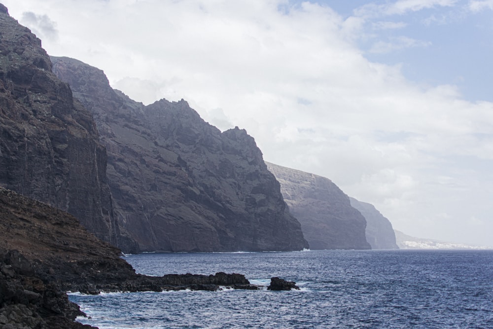 brown rocky mountain beside sea during daytime