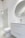 A modern bathroom interior featuring a white vanity with a sleek basin and a silver faucet. Above the vanity is a large round mirror. To the left, there's a glass-enclosed shower with a silver showerhead. The walls and floor have a minimalistic design with light, neutral colors.
