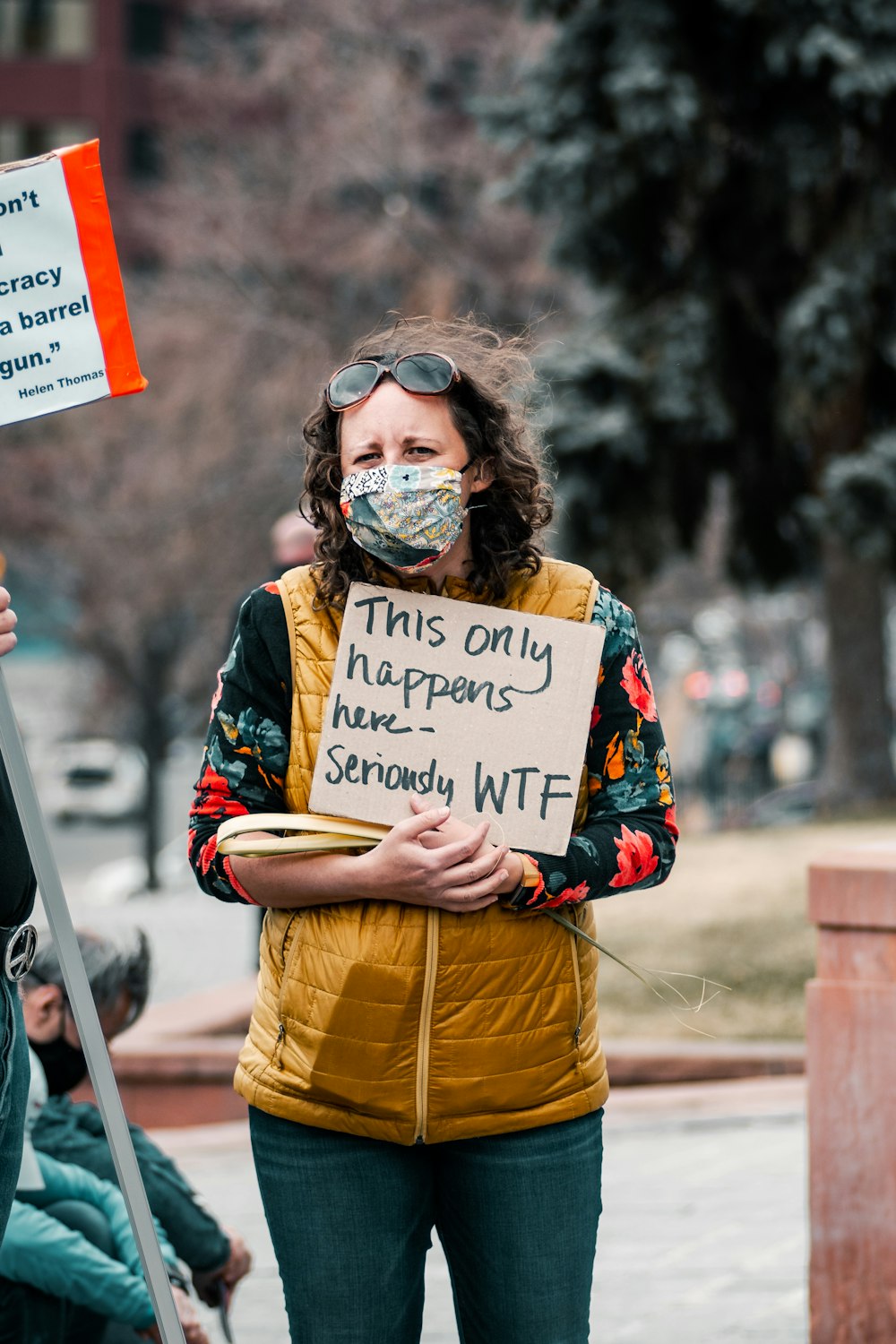 woman in yellow and blue jacket holding white and red signage