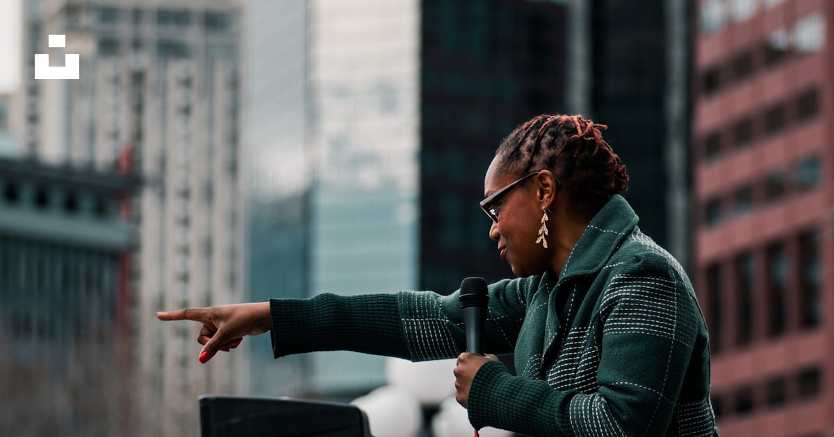 Woman In Green Jacket Standing Near Building During Daytime Photo woman-in-green-jacket-standing-near-building-during-daytime-photo