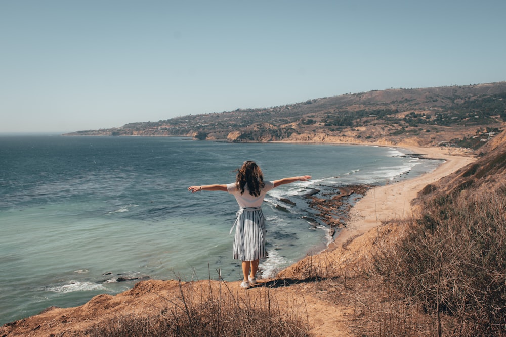 woman in white shirt standing on brown grass field near body of water during daytime