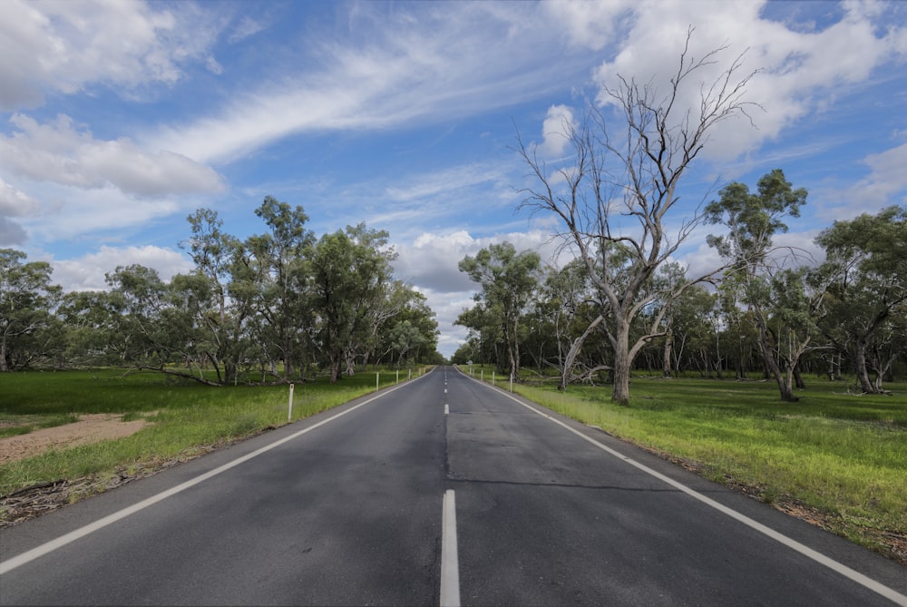 gray asphalt road between green grass field under blue and white sunny cloudy sky during daytime