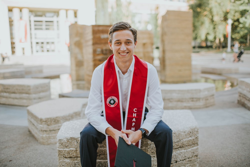 Mann in weißem Blazer und roter Krawatte sitzt auf Betonbank