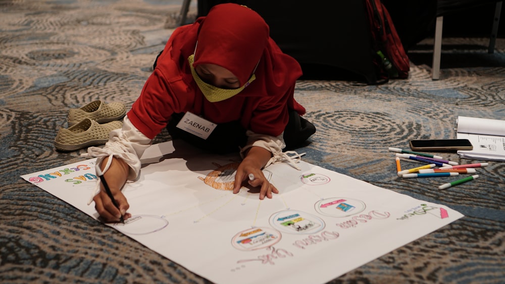 child in red knit cap and white long sleeve shirt writing on white paper