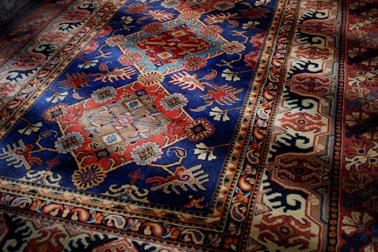 An intricately patterned rug with a dominant blue and red color scheme. The central section displays symmetrical floral designs with geometric shapes interspersed, while the border features a series of repeating motifs in complementary colors.
