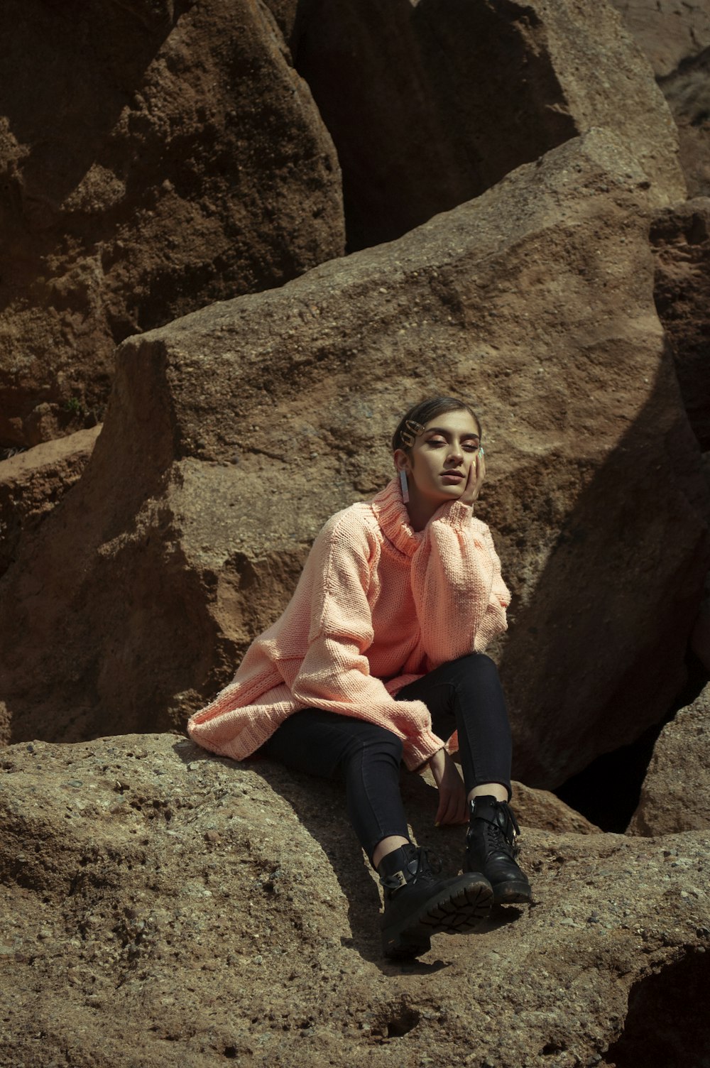 woman in pink long sleeve shirt and black pants sitting on brown rock