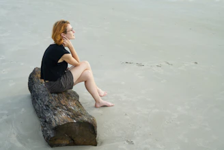 woman in black tank top sitting on gray rock by the sea during daytime