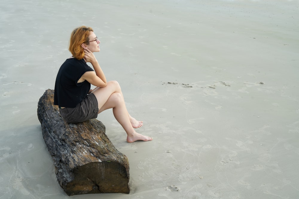 woman in black tank top sitting on gray rock by the sea during daytime