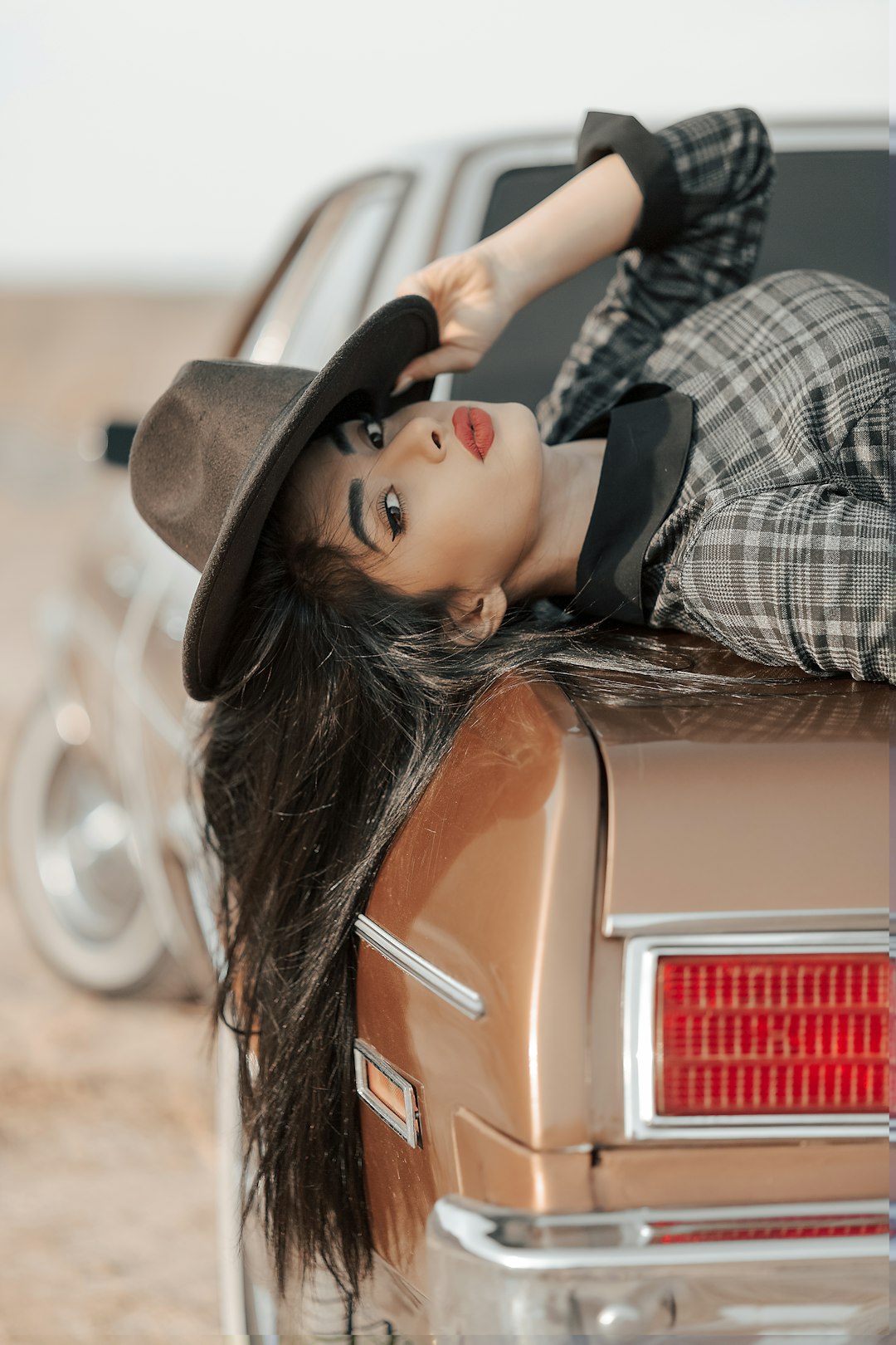 woman in black and white plaid long sleeve shirt wearing black hat leaning on brown car