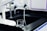A laboratory workspace features a black countertop with a beaker partly filled with liquid. Above the beaker, there is laboratory equipment including faucets and dispensers. The environment appears sterile and clean, typical of a scientific or research setting.