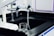 A laboratory workspace features a black countertop with a beaker partly filled with liquid. Above the beaker, there is laboratory equipment including faucets and dispensers. The environment appears sterile and clean, typical of a scientific or research setting.