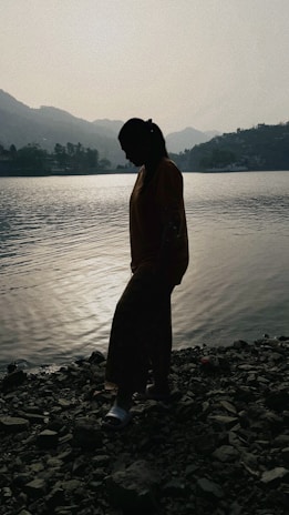 A silhouette of a lone figure standing at the edge of a mist-covered lake at twilight.
