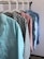 Several colorful shirts hang in a row on white hangers against a light-colored wall. Each shirt features a distinct pattern, including chevrons, stars, solid pink, floral designs, and small stars.