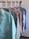 Several colorful shirts hang in a row on white hangers against a light-colored wall. Each shirt features a distinct pattern, including chevrons, stars, solid pink, floral designs, and small stars.