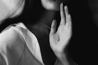 A close-up shot of hands holding an aged bronze pendant, softly illuminated in grayscale.