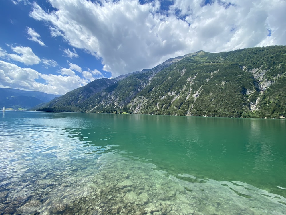 green lake near green mountain under blue sky during daytime