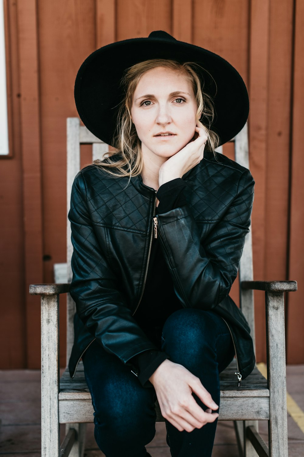 woman in black leather jacket and blue denim jeans sitting on brown wooden chair