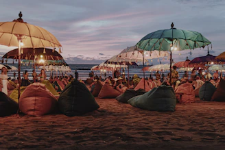 Sunset party on the beach with people dancing under colorful lights.