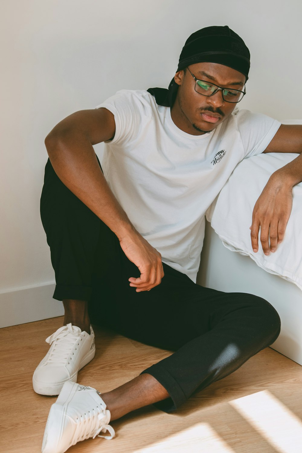 man in white nike crew neck t-shirt and black pants sitting on brown wooden floor