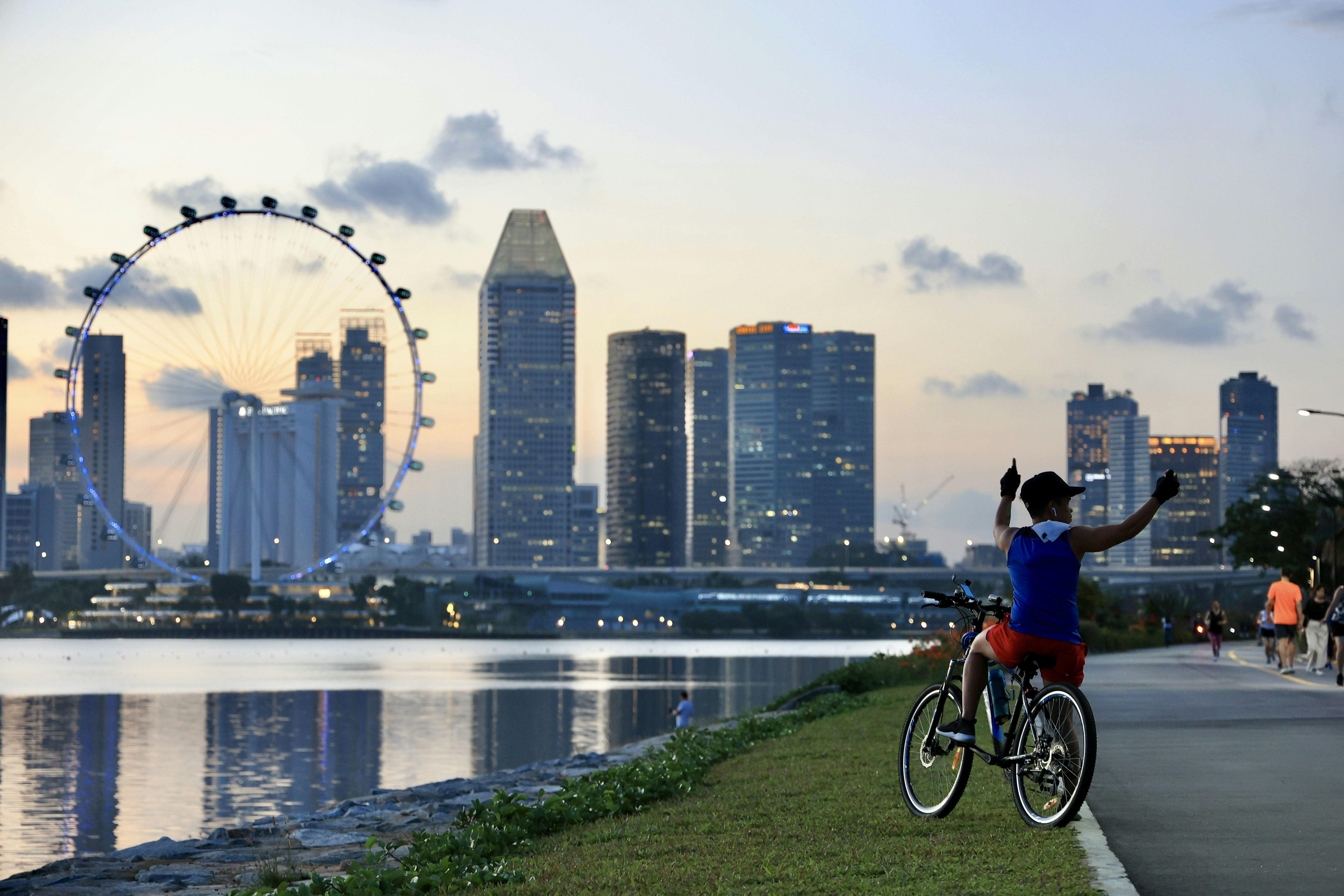 man in blue shirt riding bicycle on green grass field near city buildings during daytime
