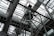 An industrial interior filled with metal beams and supports, showcasing a complex structure of girders and railings. The ceiling is comprised of glass panels allowing natural light to illuminate the space. The architectural design features intricate and heavy-duty construction elements.
