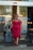 A person wearing a red dress and sunglasses is walking out of a hotel entrance with a suitcase in one hand and a phone in the other. The entrance features a glass door with the hotel logo 'park inn' visible.