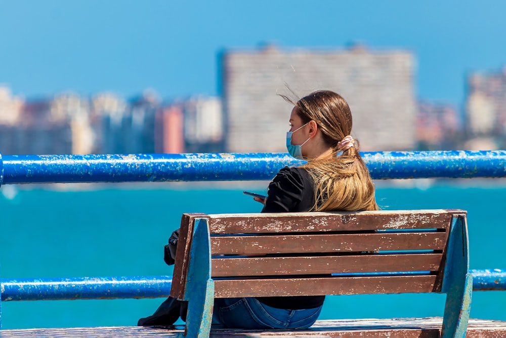 woman in black jacket sitting on brown wooden bench during daytime