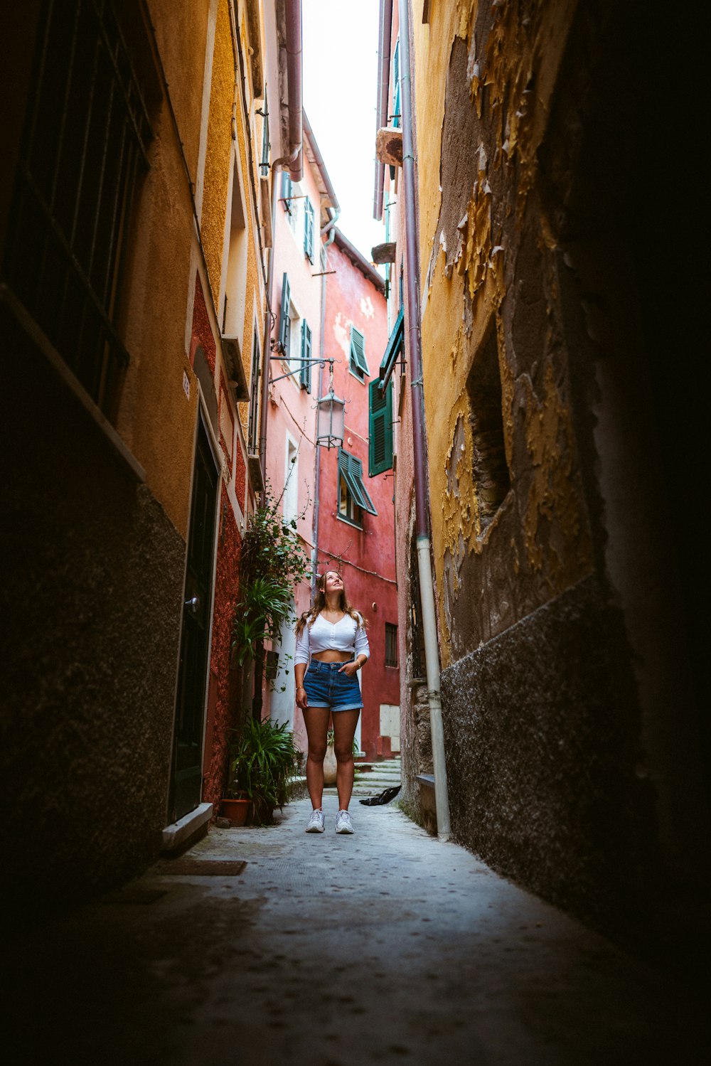 woman in white shirt and blue denim shorts walking on pathway between brown concrete buildings during