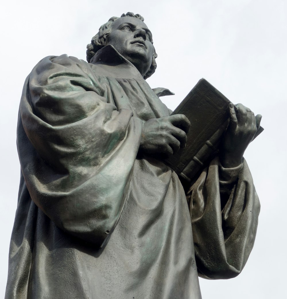 man in coat holding book statue