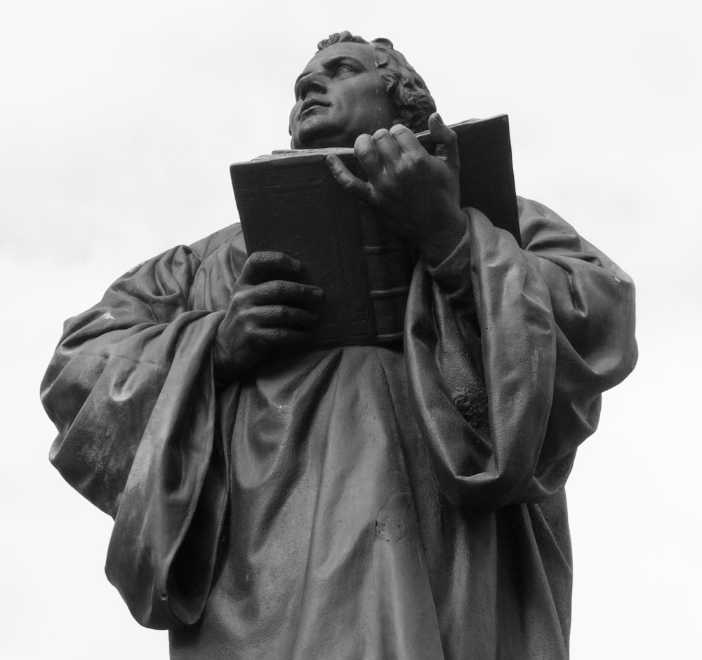 grayscale photo of woman holding book statue
