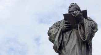 man holding book statue under white clouds during daytime
