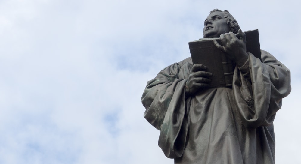 hombre sosteniendo estatua de libro bajo nubes blancas durante el día