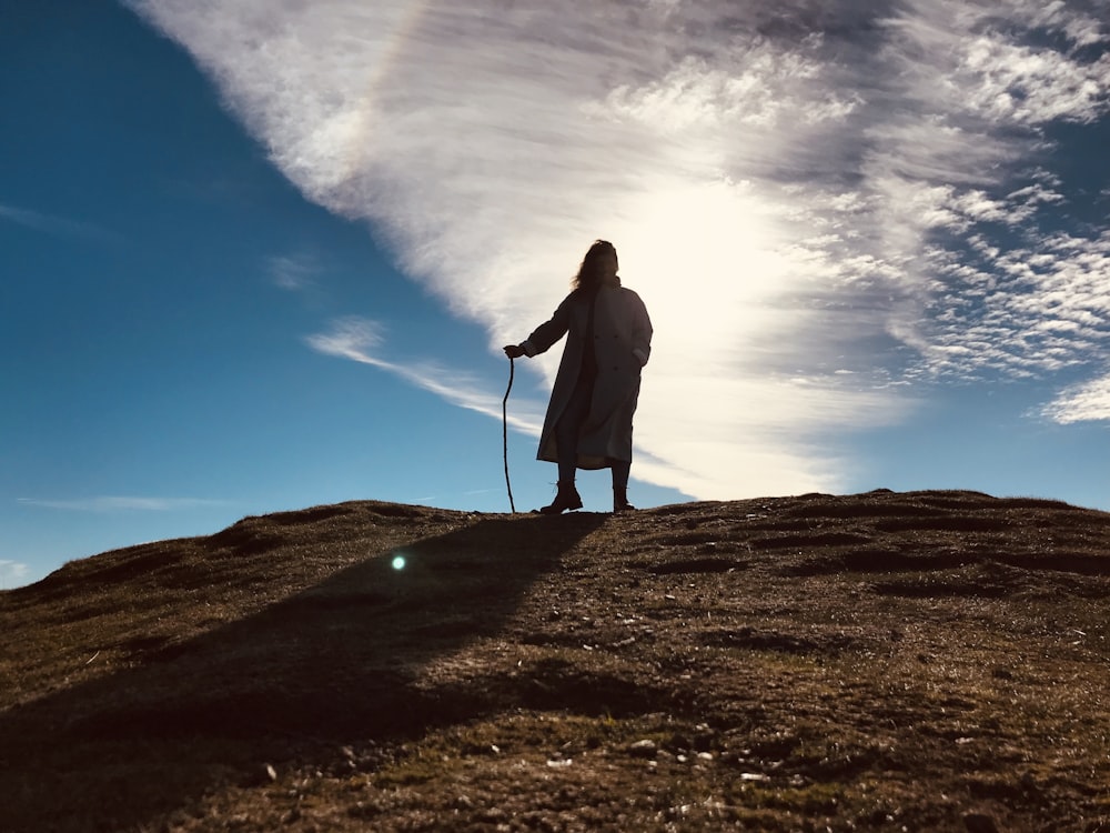 mulher no casaco preto de pé no campo marrom sob o céu nublado ensolarado azul e branco durante