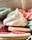 A close-up view of colorful, decorative meringue cookies and biscuits. The meringues are pastel-colored in shades of green, pink, and white, with intricate swirling patterns. One biscuit is visible with white icing and pink decorative elements on top.