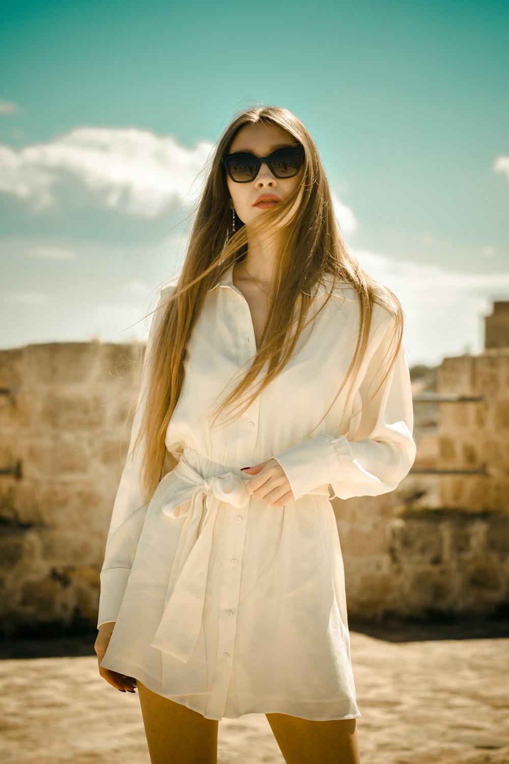 Femme en robe blanche à manches longues portant des lunettes de soleil noires