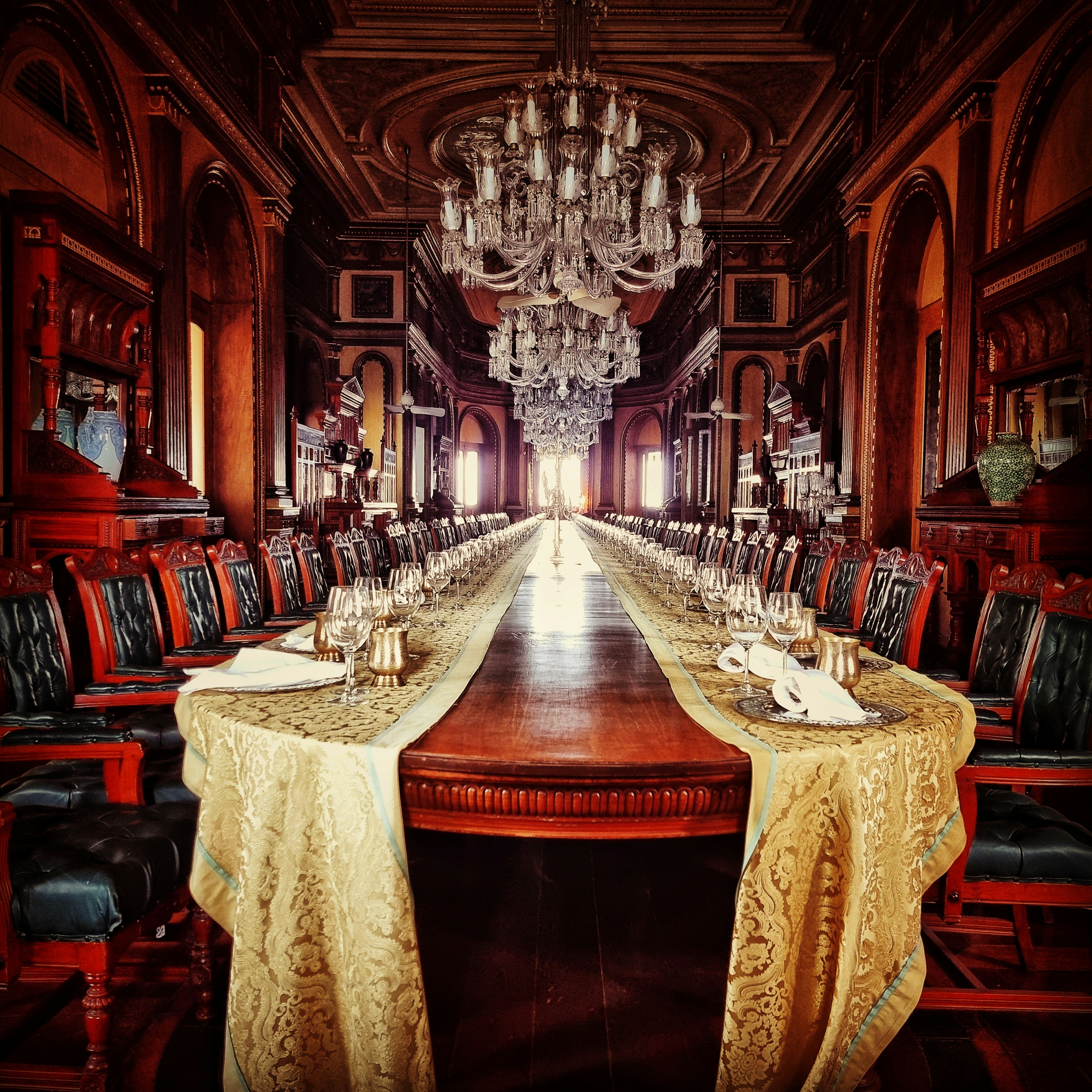 Grand palace dining hall with crystal chandeliers, white tablecloths, candlelight, ornate gilded pillars, warm amber atmosphere