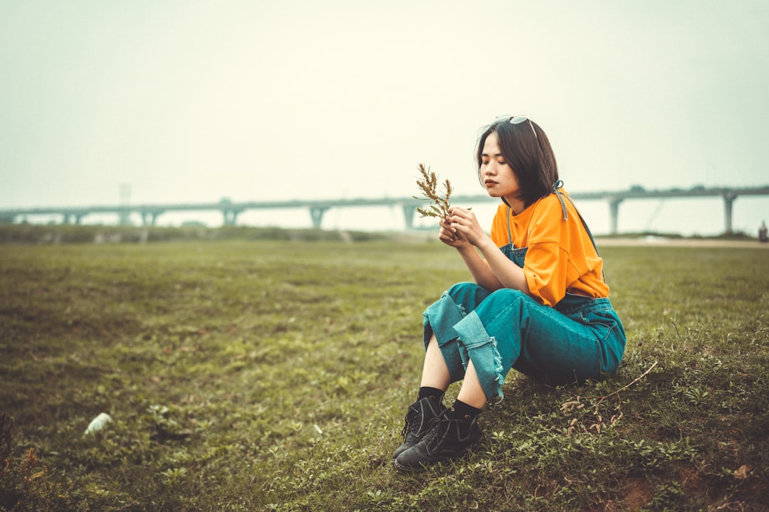 woman in yellow shirt and blue denim jeans sitting on green grass field during daytime