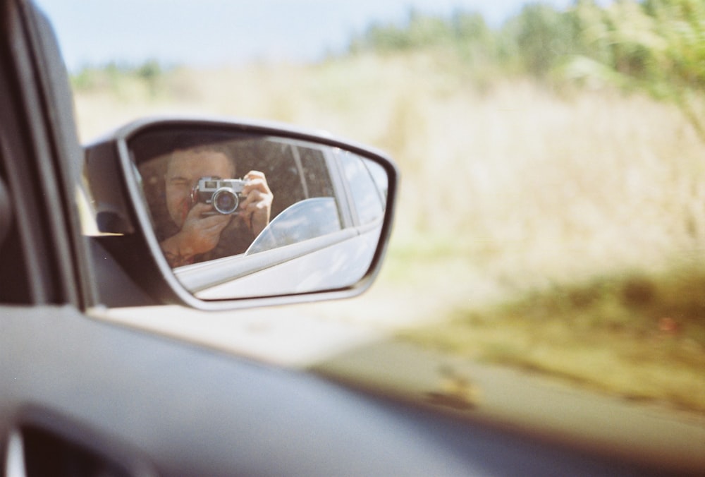 man in black sunglasses taking selfie in car side mirror