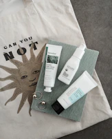 A stylish flat lay of luxury LV bags, sunglasses, and a sun emoji sticker on a sandy beach towel.