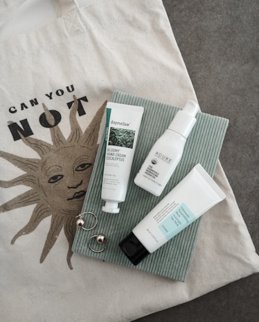 A minimalist flat lay of enjoyla’s signature tote bag, tumbler, and t-shirt with nature background.