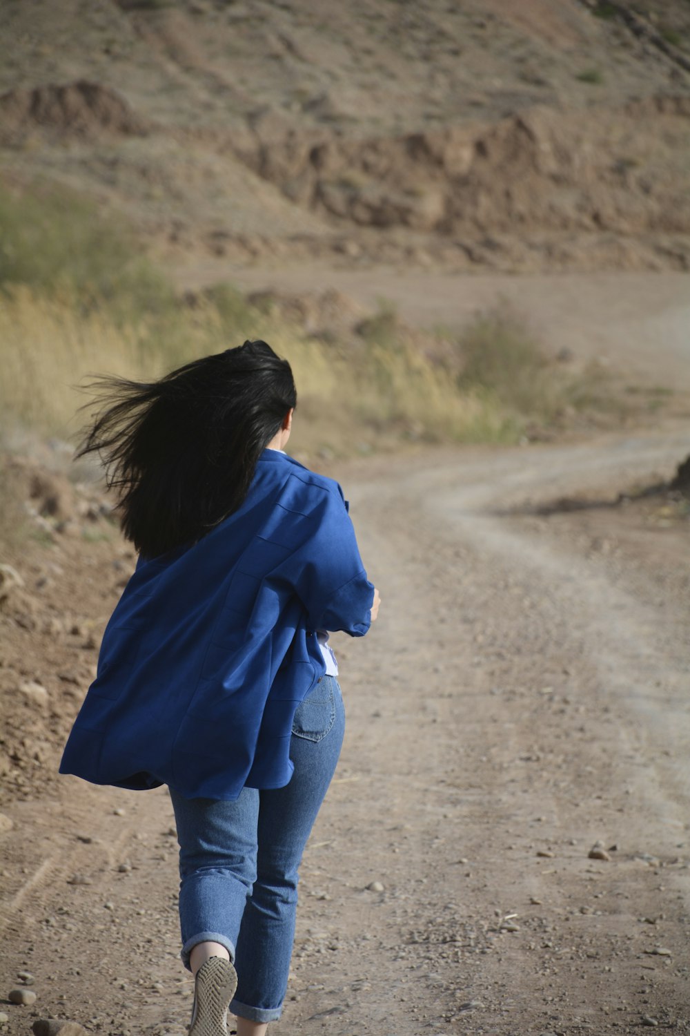 woman in blue hoodie and blue denim jeans walking on dirt road during daytime