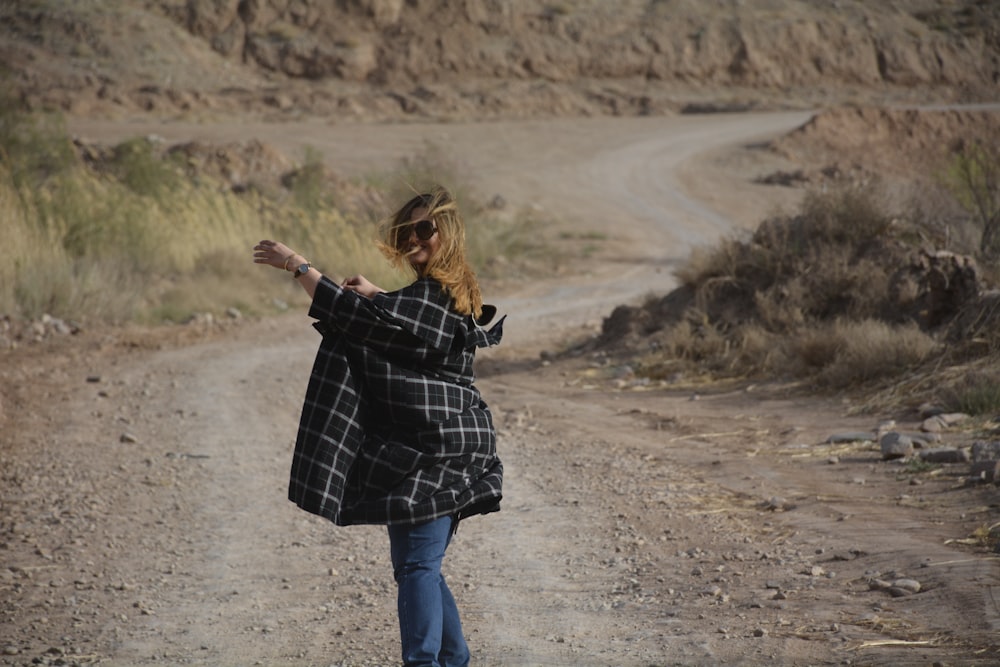 woman in black and white checkered coat and blue denim jeans standing on dirt road during