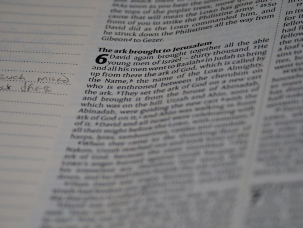 A close-up view of an open book with visible text. The page appears to be from the Bible, particularly featuring a passage with a large number '6' and a chapter title 'The ark brought to Jerusalem'. There is handwritten text in the left margin of the page.